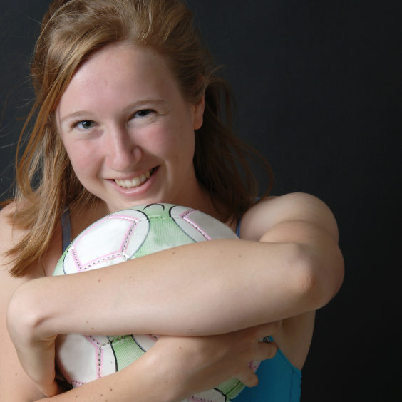 Portrait of a teen girl hugging a soccer ball, isolated against a black background.